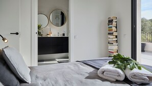A bedroom with a bed, a bedside table, a mirror, a stack of books, and a view of the outdoors. - Villa Casa Selva - Luxury and nature only 7 minutes drive from Sitges (Sitges)
