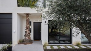 Une maison moderne à deux étages, avec une porte noire, un pilier en pierre et un grand arbre dans le jardin.