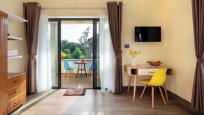 A modern hotel room with a desk, chair, TV, and a balcony with outdoor seating. - Ha Blue Villa - Hoi An (Da Nang)