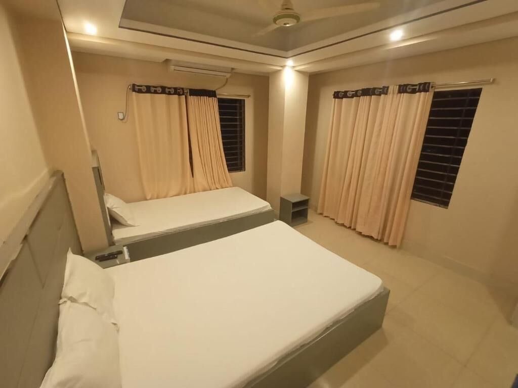 A hotel room with two beds, beige curtains, a ceiling fan, and a small table.