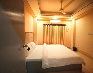 A hotel room with a bed, a ceiling fan, a nightstand, and a window with curtains. - Hotel Grand Usman Sylhet (Sylhet)