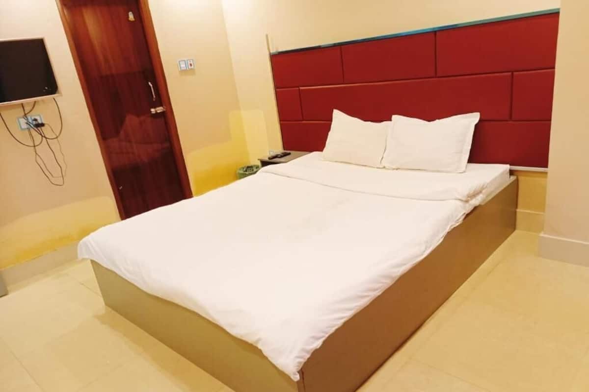 Un lit avec une tête de lit rouge, du linge de lit blanc et une table de chevet avec une lampe.