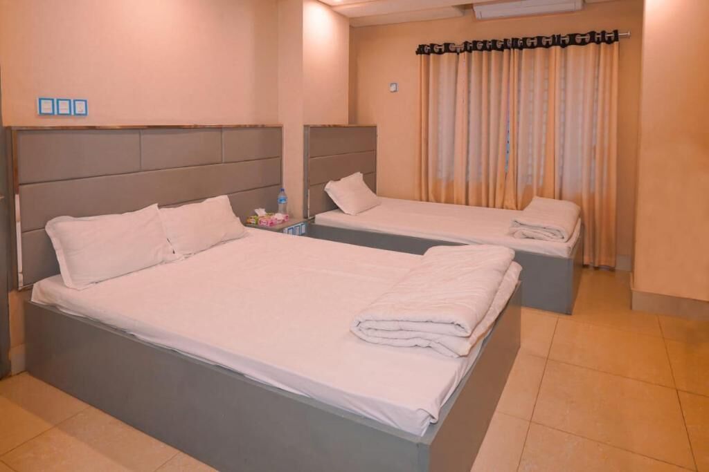 Habitación de hotel con dos camas, una mesita con una botella y pañuelos, y una cortina estampada.
