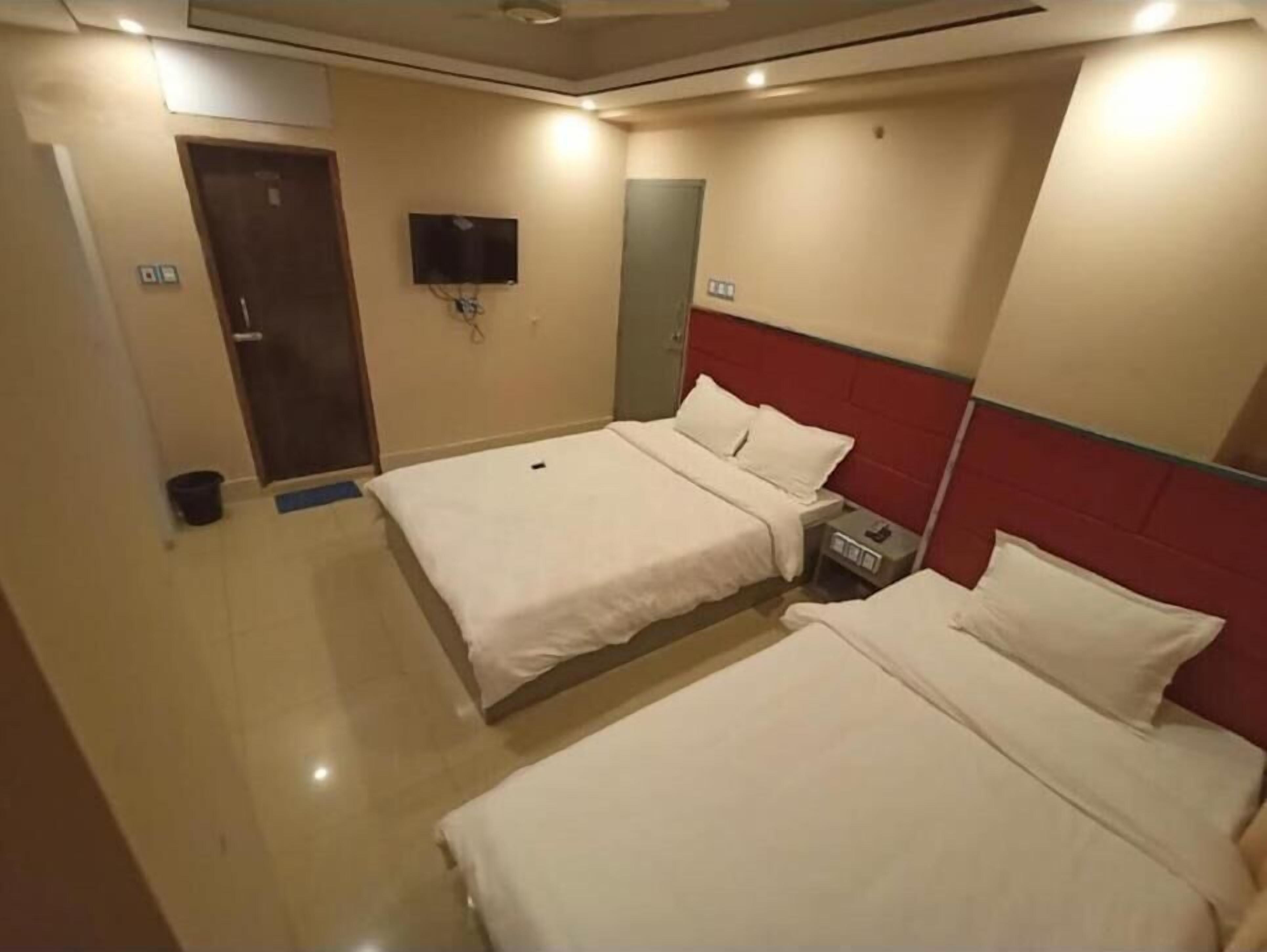 Ein Hotelzimmer mit zwei Betten, einem an der Wand befestigten Fernseher und einer Tür.
