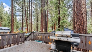 A deck with a grill, surrounded by tall trees.