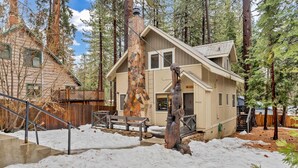 A cabin with a stone chimney, wooden deck, and a staircase leading to the entrance.