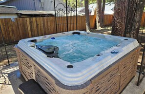 Jacuzzi en un patio trasero con valla de madera y árboles.