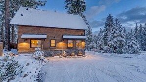 Eine Holzhütte mit schneebedecktem Dach, umgeben von schneelastigen Bäumen.