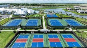 A tennis court complex with multiple courts, surrounded by greenery and a body of water. - Chic and elegant waterfront home in Lorraine Lakes - Patsgang (Bradenton)
