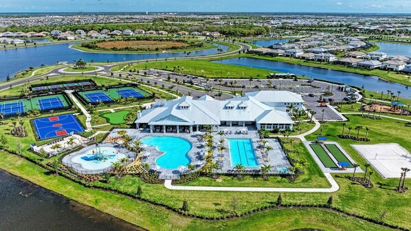 An aerial view of a residential area with a large building featuring a swimming pool, tennis courts, and a landscaped park. - Chic and elegant waterfront home in Lorraine Lakes - Patsgang (Bradenton)