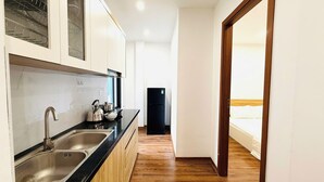 Ein schmaler Flur mit einer Küchenzeile links, die ein Spülbecken, ein Herd und Schränke umfasst. In der Ferne ist ein Kühlschrank zu sehen.