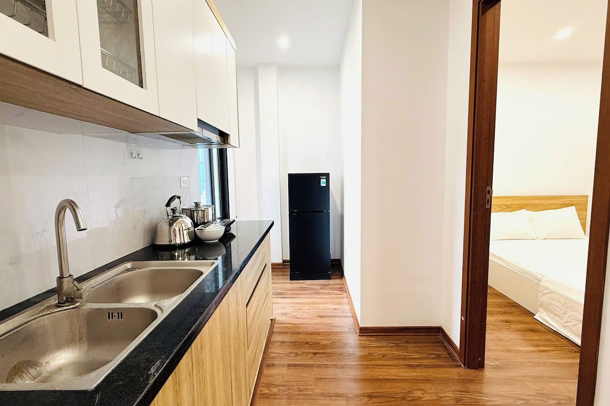 Una cocina compacta con lavamanos, hervidor y refrigerador negro.