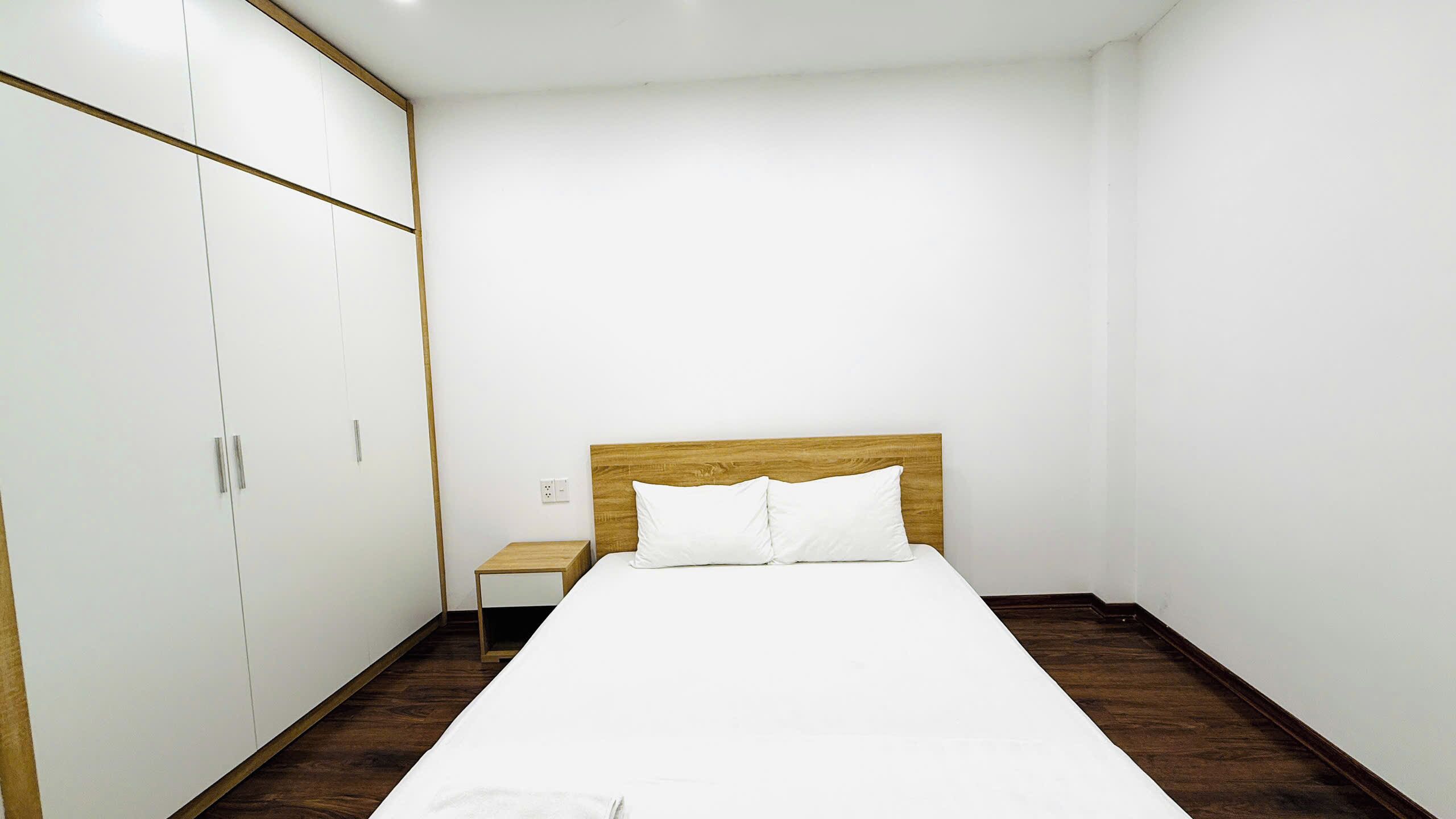 A bedroom with a bed, wooden headboard, white walls, and a wardrobe.