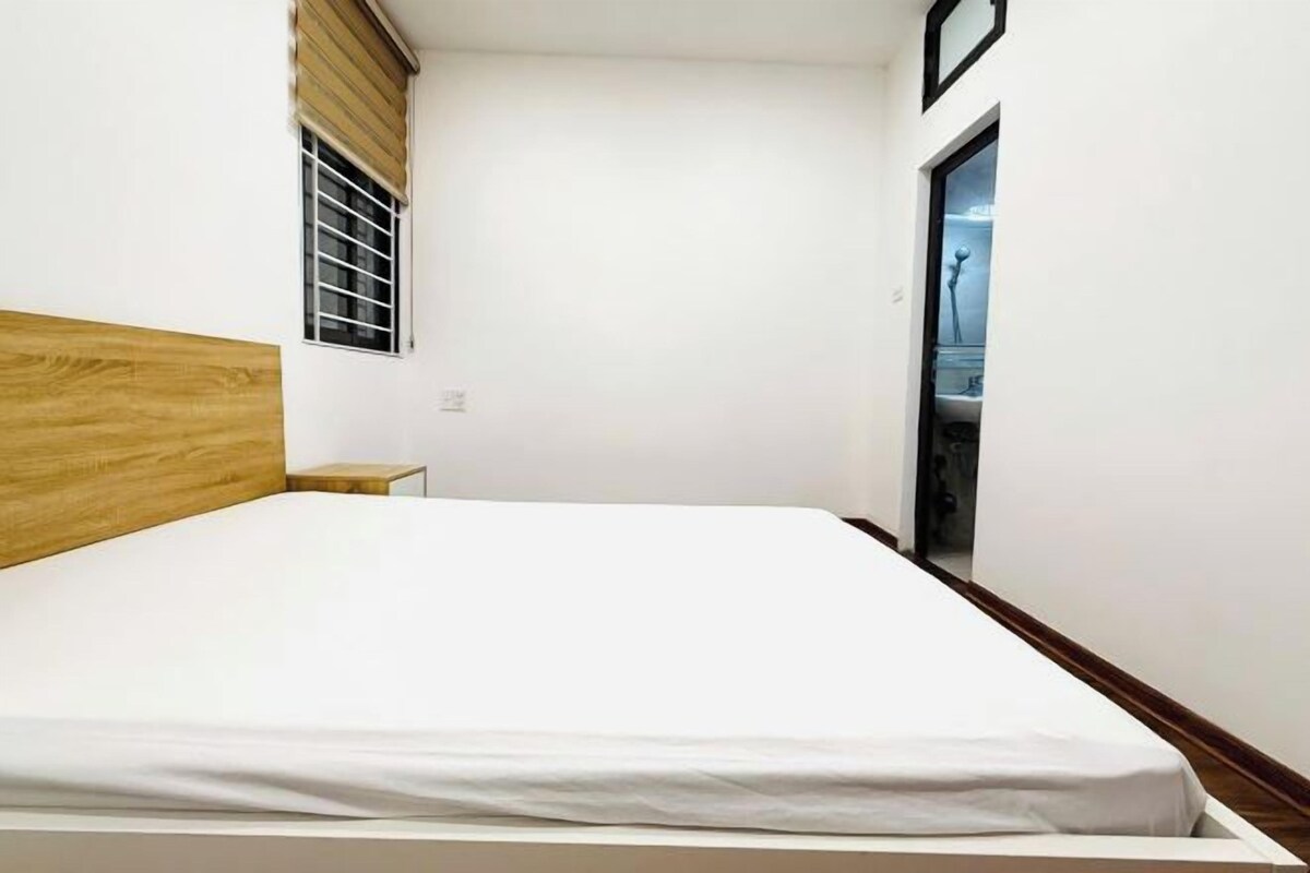 Ein Schlafzimmer mit hölzernem Kopfteil, einem Einzelbett, einem kleinen Nachttisch und einem Fenster mit Jalousien.