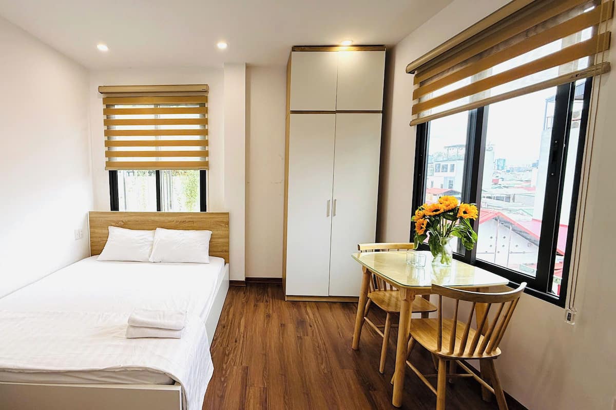 Una habitación de hotel con una cama, una mesa con sillas, una ventana con persianas y un armario.