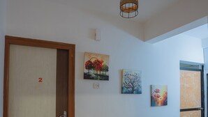 En hall med en dörr i trä märkt med siffran ’2’, en taklampa och tre tavlor på väggen.