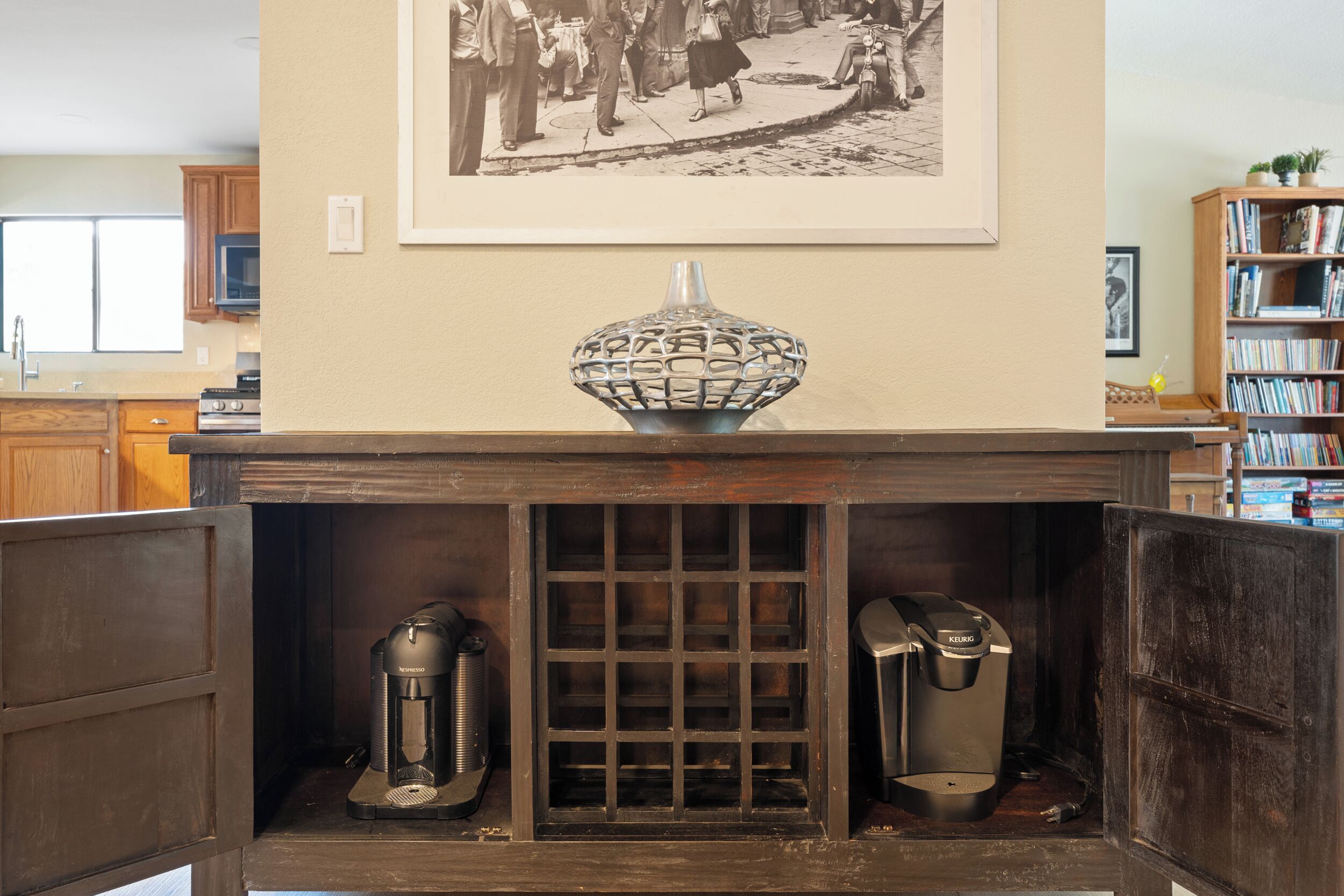Una chimenea con un cuenco decorativo, dos cafeteras y una fotografía en blanco y negro enmarcada sobre ella.