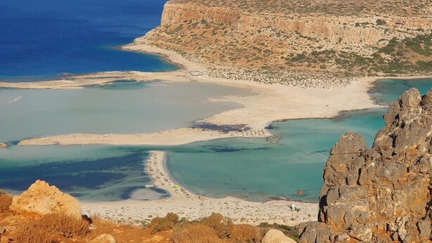 Un paysage côtier caractérisé par des falaises rocheuses, une eau d’un bleu limpide et une plage de sable.
