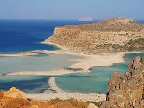 A coastal landscape with rocky cliffs, clear blue waters, and a sandy beach.