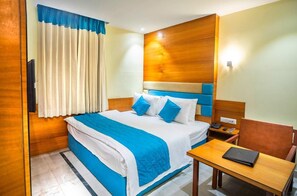 A hotel room with a bed, a desk, a chair, a nightstand, and a wall-mounted TV.