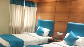 A hotel room with two beds, each with a blue headboard, white bedding, and blue and white striped blankets. There is a wooden headboard, a nightstand with a phone, and a window with curtains. - King S Crown (Barasat)