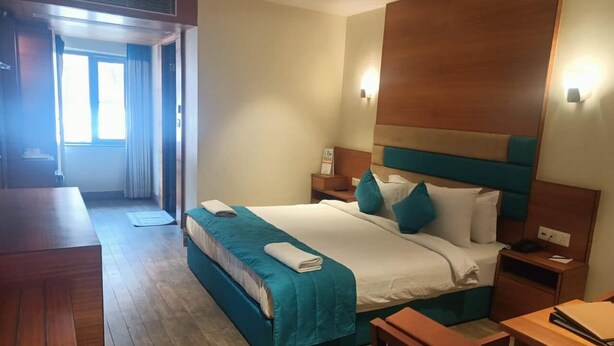 A hotel room with a bed, bedside tables, a desk, and a window. - King S Crown (Barasat)