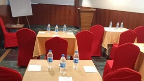A conference room with tables covered in beige tablecloths, red chairs, and water bottles on each table. - King S Crown (Barasat)
