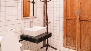 Bagno con pareti piastrellate in bianco, un water bianco, una porta in legno e un lavandino nero su un supporto in legno.