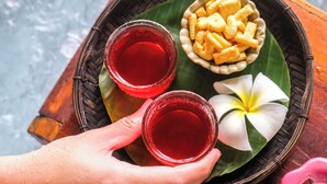 Un vassoio con due bicchieri di liquido rosso, una ciotola di snack e un fiore su una foglia.