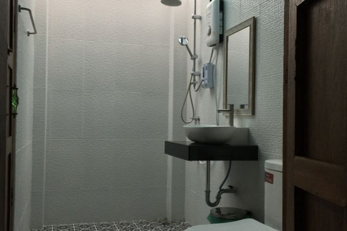 A small bathroom with a white sink, a mirror, and a shower head.