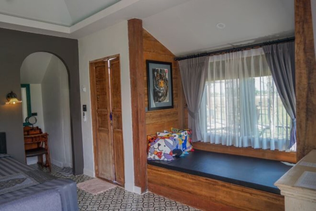 A room with a bed, a wooden bench by the window, a framed picture, and a mirror.
