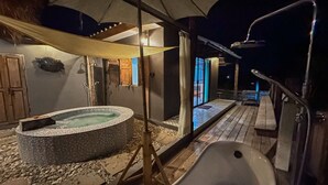 Una vasca idromassaggio e un angolo doccia con un pavimento in legno e una zona relax coperta.