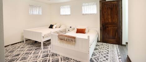 A bedroom with two single beds, a wooden door, and patterned carpet.