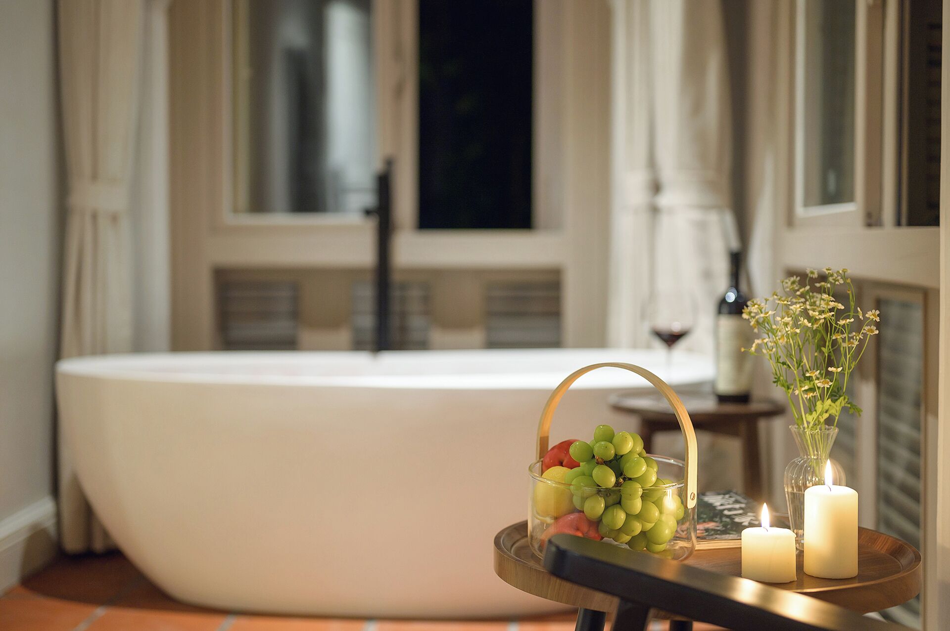 A bathroom with a bathtub, a glass bowl with fruits, candles, and a vase with flowers.