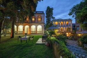 Un cortile con zona pranzo, un albero grande e un edificio con finestre ad arco e balconi.