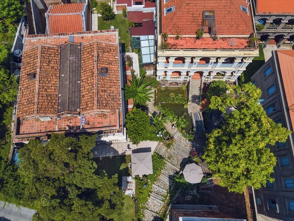 An aerial view of a building with a red-tiled roof, surrounded by greenery and adjacent buildings. - White House Monet Garden Coffee (Xiamen)