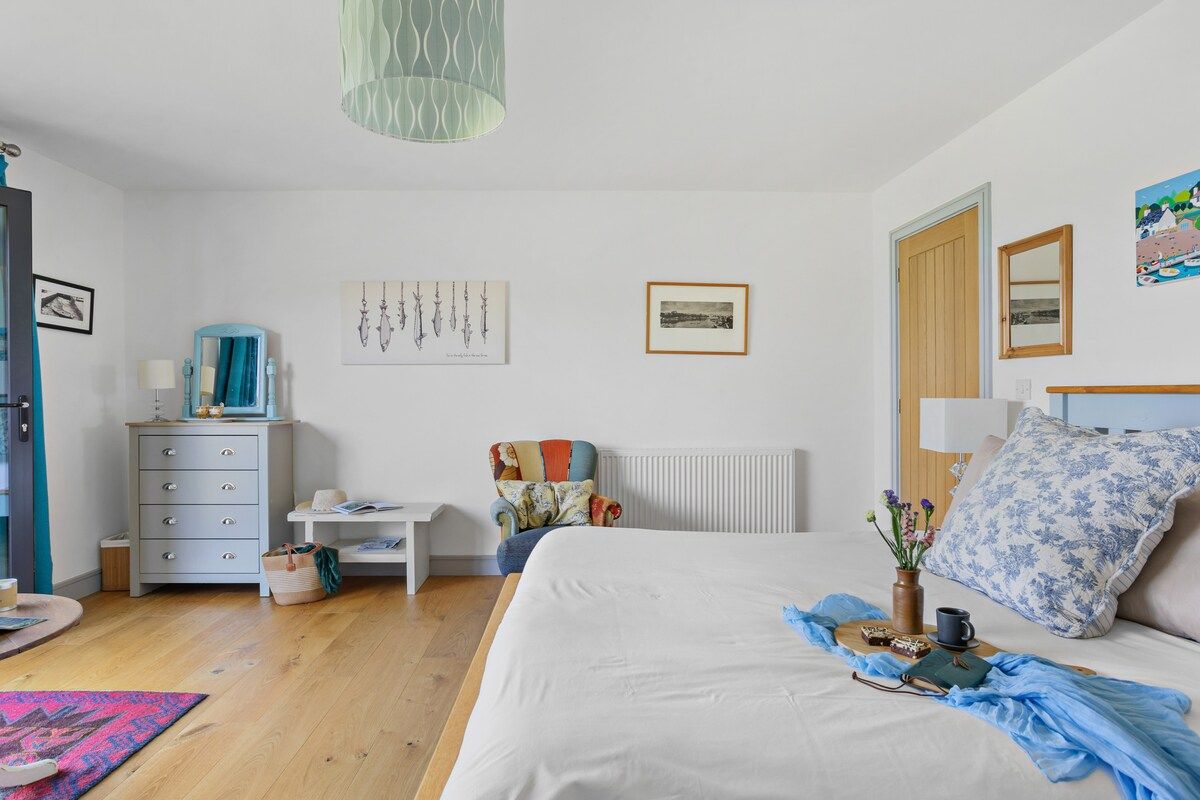 Une chambre à coucher avec un lit, une commode, une chaise et des œuvres d’art accrochées aux murs.