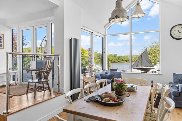 A spacious dining area with a wooden table, chairs, and a view of the outdoors through large windows.