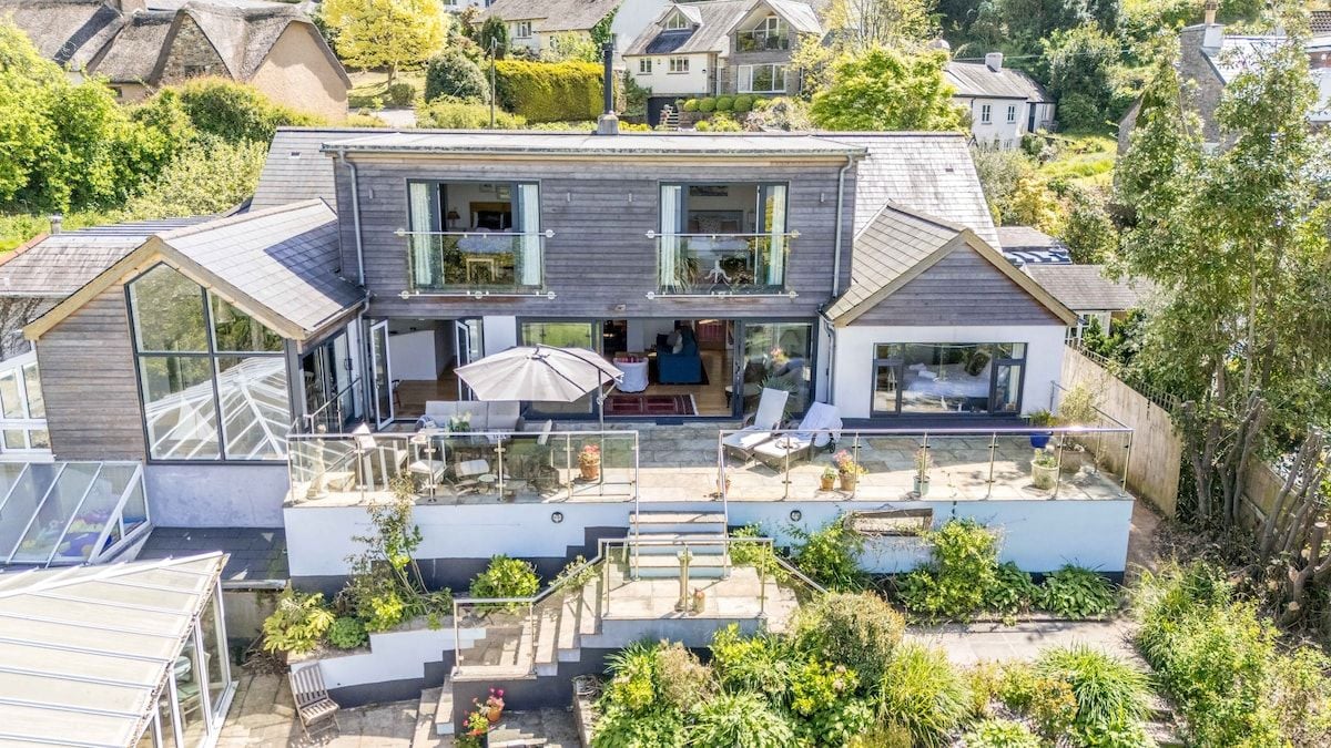 Een modern herenhuis met twee verdiepingen, een ruim balkon, een overdekt terras en een trap naar de bovenverdieping.