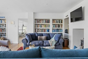 Een woonkamer met een blauwe bank, een boekenkast en een flatscreen televisie.