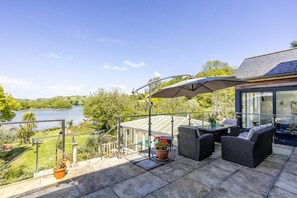 Een balkon met buitenmeubilair, een glazen omheining en uitzicht op een meer.
