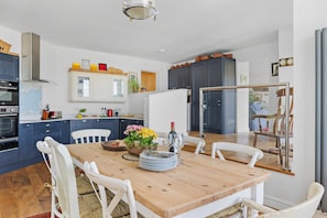Una cucina moderna con un tavolo da pranzo in legno, sedie bianche e diversi elettrodomestici.