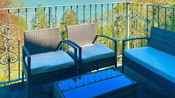 A balcony with wicker furniture and a glass table overlooking a body of water. - Shanklin Stunning Sea Views (Shanklin)