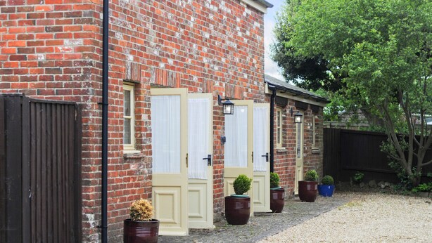 A brick building with three doors, each with a window above. There are potted plants in front of the doors. - The Hayloft (Queen Bower)