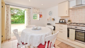 A kitchen with a dining table, chairs, a stove, and a window with curtains. - The Hayloft (Queen Bower)
