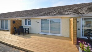 Un bâtiment doté d’un toit recouvert de tuiles, de grandes portes-fenêtres coulissantes, d’une terrasse en bois et d’un petit espace extérieur aménagé pour s’asseoir.
