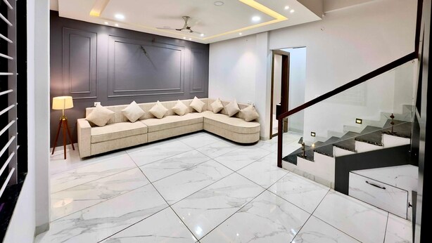 A modern living room with a sectional sofa, a glass staircase, and a marble floor.