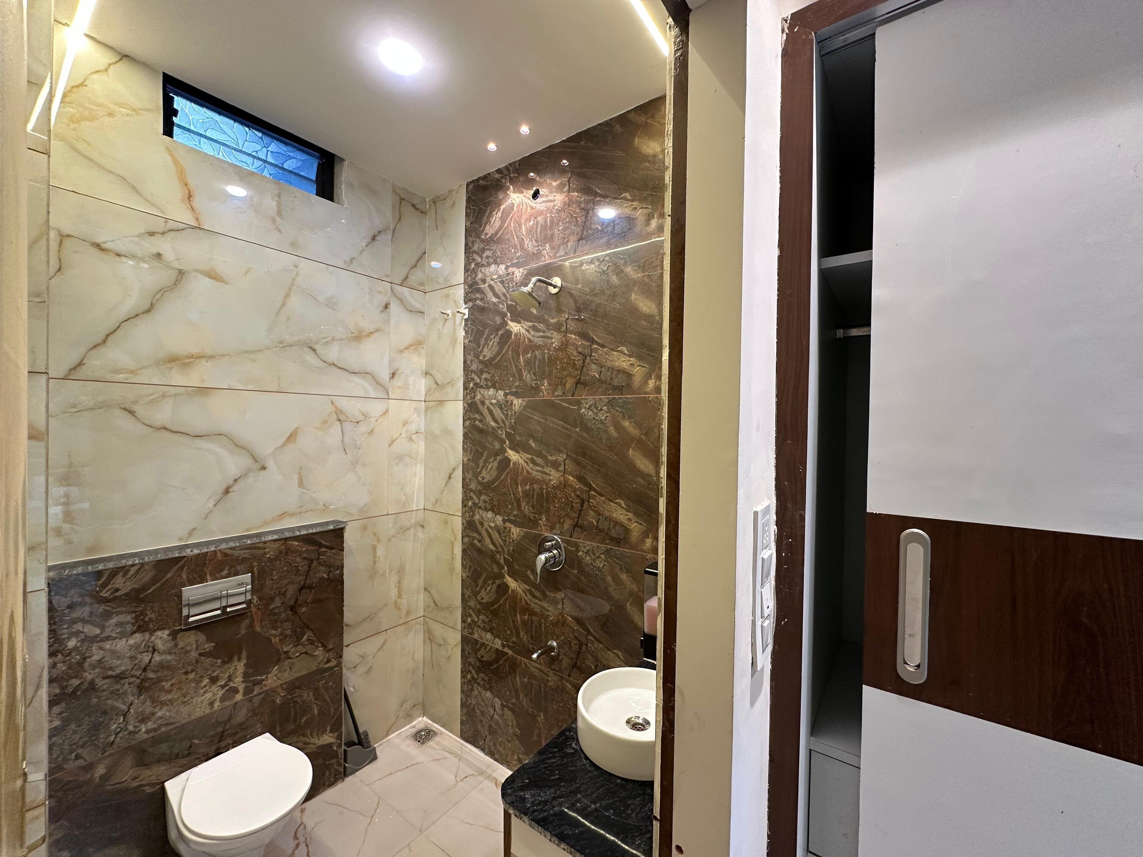 A bathroom with marble walls, a toilet, a sink, and a shower area.