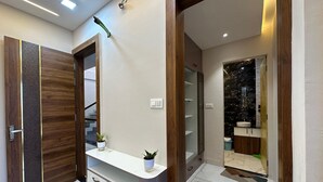 A modern bathroom with a marble floor, a wooden vanity, a large mirror, and a black tiled wall.