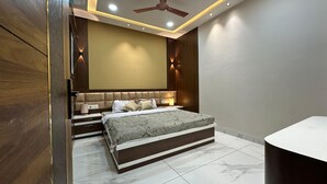A modern bedroom with a large bed, a ceiling fan, recessed lighting, and a wooden accent wall. - Luxury 3bhk villa perfect for families and friends with a rooftop party hall (Indore)